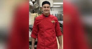 Chef in red jacket in kitchen.