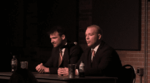 Two men in suits at a panel discussion.