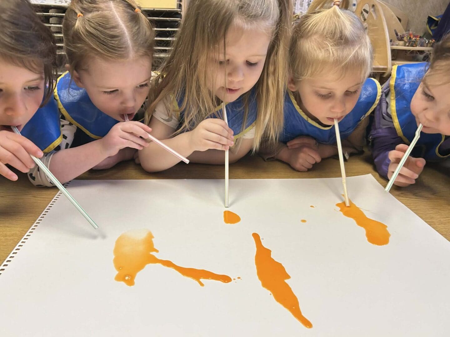 Children painting with straws and orange paint.