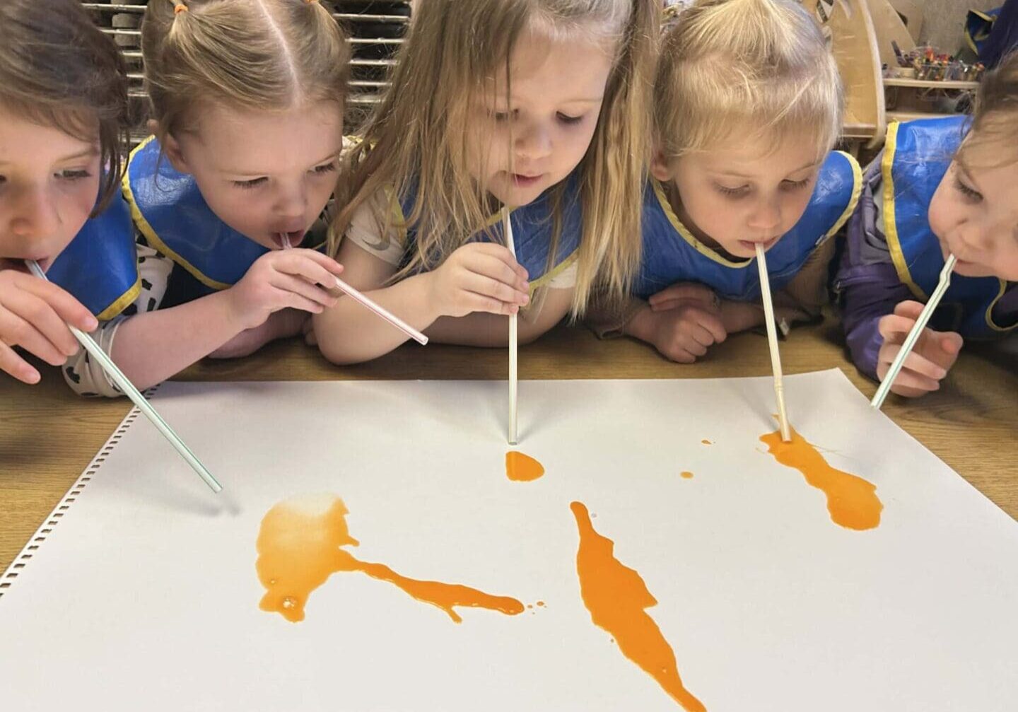 Children painting with straws and orange paint.